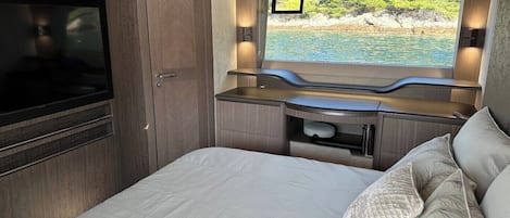 A compact bedroom with a bed, a TV, a window with a view of the sea, and built-in storage.