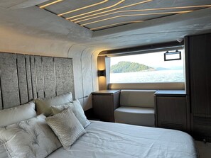 Un interior moderno con una cama, zona de estar y ventana con vistas al agua y colinas.