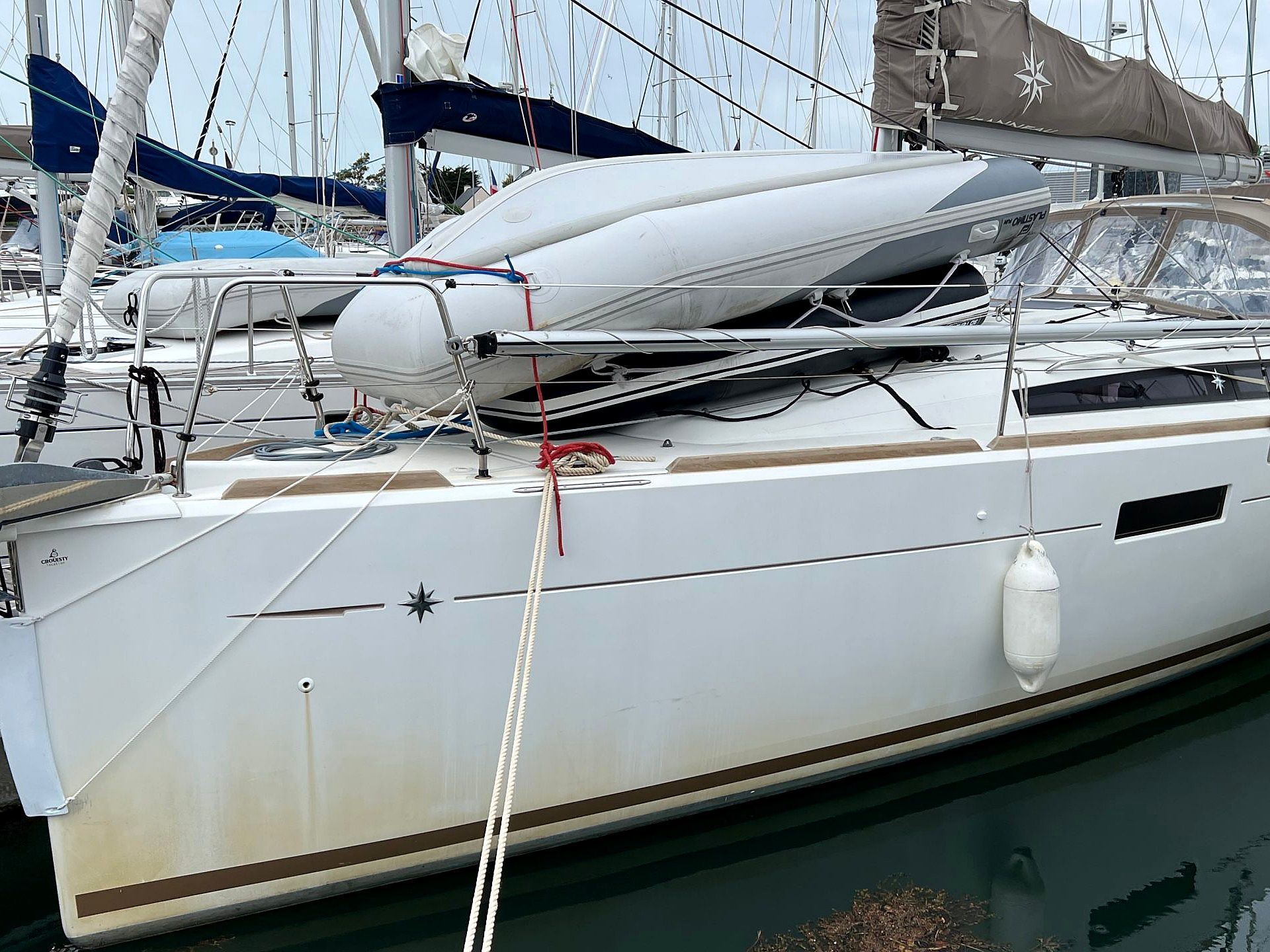 Un voilier était amarré dans une marina, avec un gréement bien visible et un emblème en forme d’étoile sur la coque.