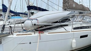 Eine Segelyacht liegt im Hafen festgemacht, mit einer geschützten Cockpitkabine, einem weißen Rumpf und einem Anker auf der Steuerbordseite.
