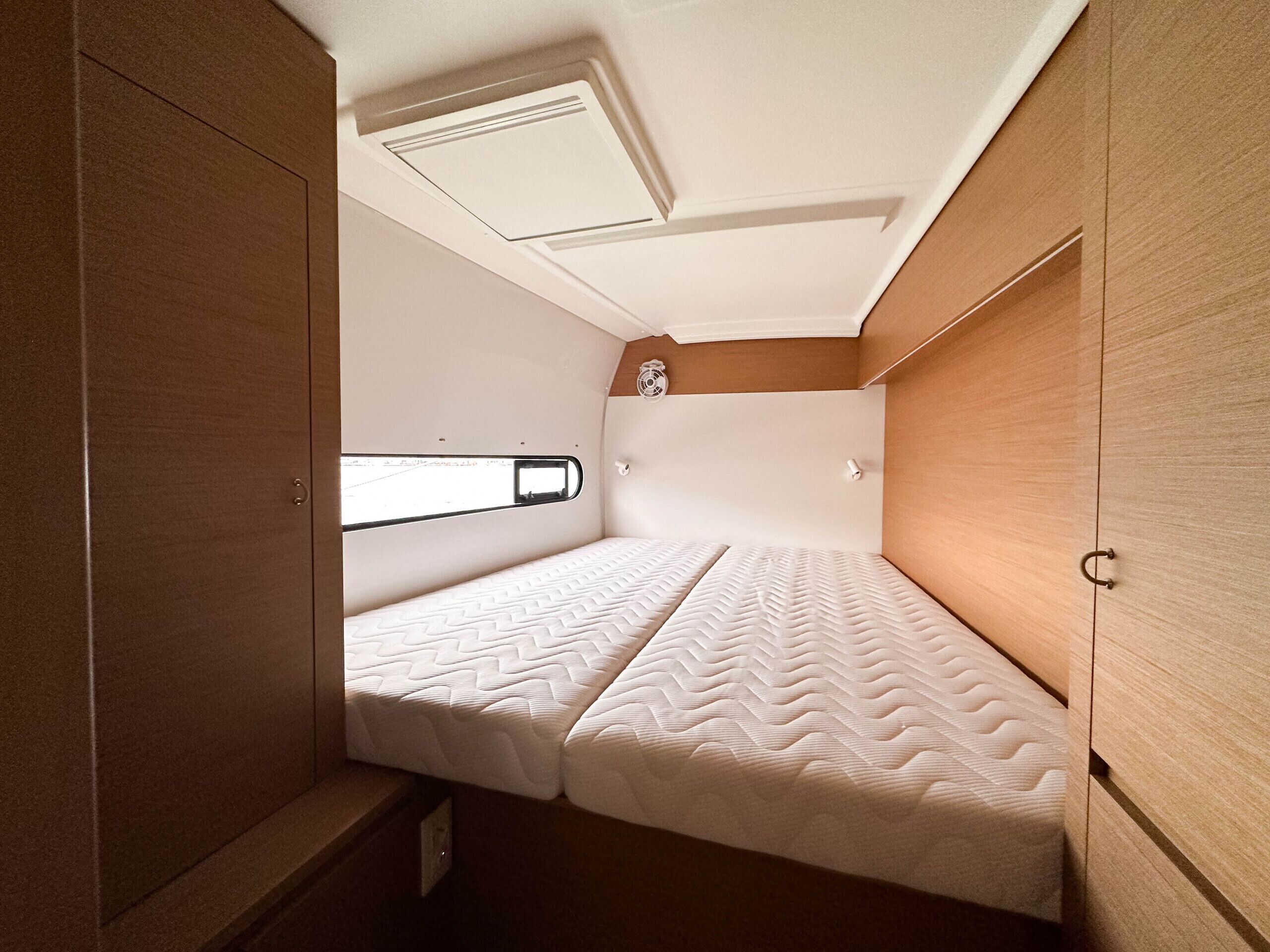 Een kleine, goed verlichte kamer met een eenpersoonsbed, een klein raam en een klok aan de muur.