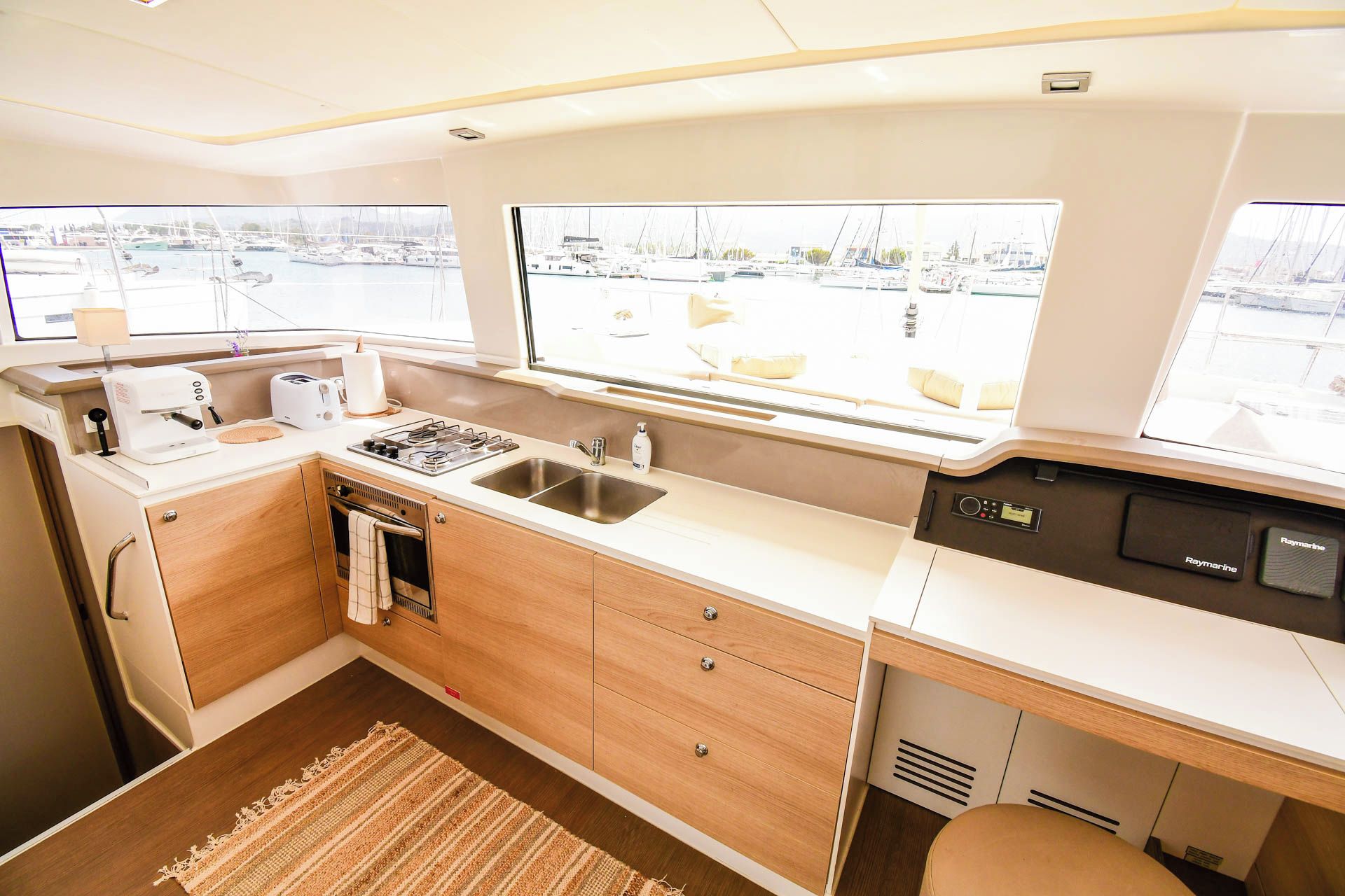 A compact kitchen with a stove, sink, and a view of a marina through large windows.