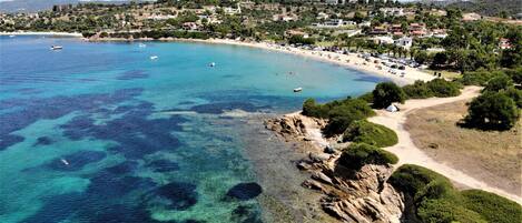 A coastal town with clear blue waters, rocky shoreline, and a beach area with visible buildings and greenery.