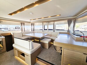 A yacht interior with a dining area, seating, a kitchen, and large windows offering views of the marina. - Sun-kissed Sailing Adventure in Split-Dalmatia, Croatia (Seget Donji)