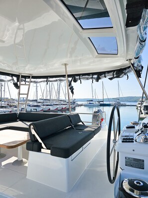 A boat deck with a covered seating area, a steering wheel, and a view of other boats in the marina. - Sun-kissed Sailing Adventure in Split-Dalmatia, Croatia (Seget Donji)