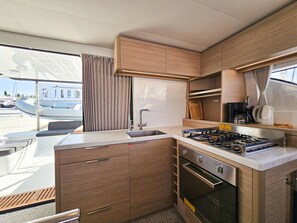 A compact kitchen with a gas stove, oven, and a window overlooking a marina. - Sun-kissed Sailing Adventure in Split-Dalmatia, Croatia (Seget Donji)