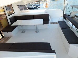 Het dek van een boot met een witte tafel, zwart gestoffeerde zitplaatsen en uitzicht op andere boten in de jachthaven.
