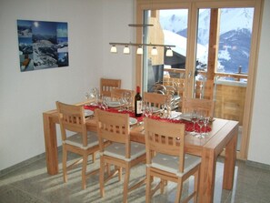 Zona de menjador amb taula de fusta preparada per a sis, amb cadires al voltant i vista a les muntanyes per la finestra.