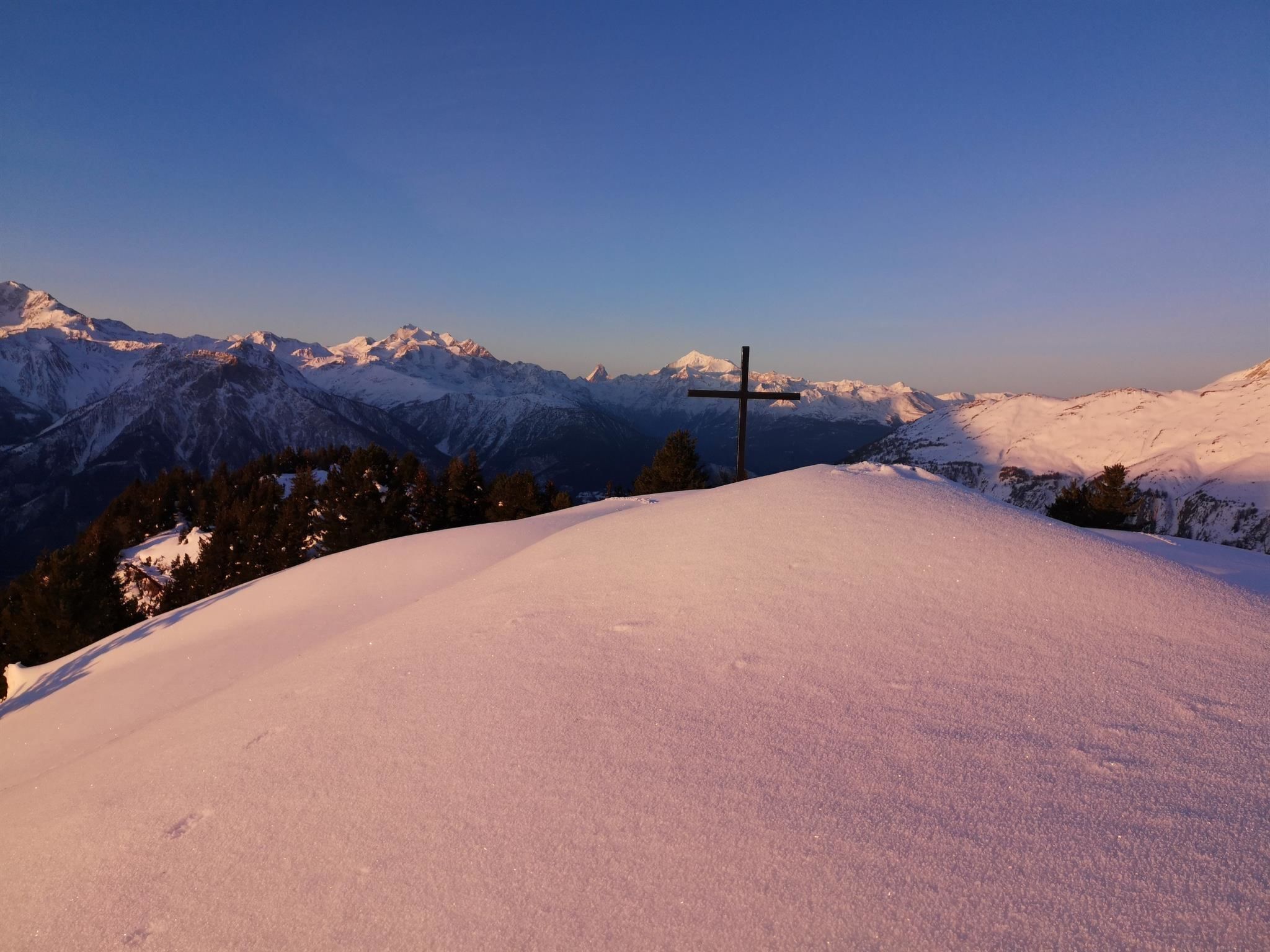 Un paysage de montagne enneigé, avec une croix au premier plan.