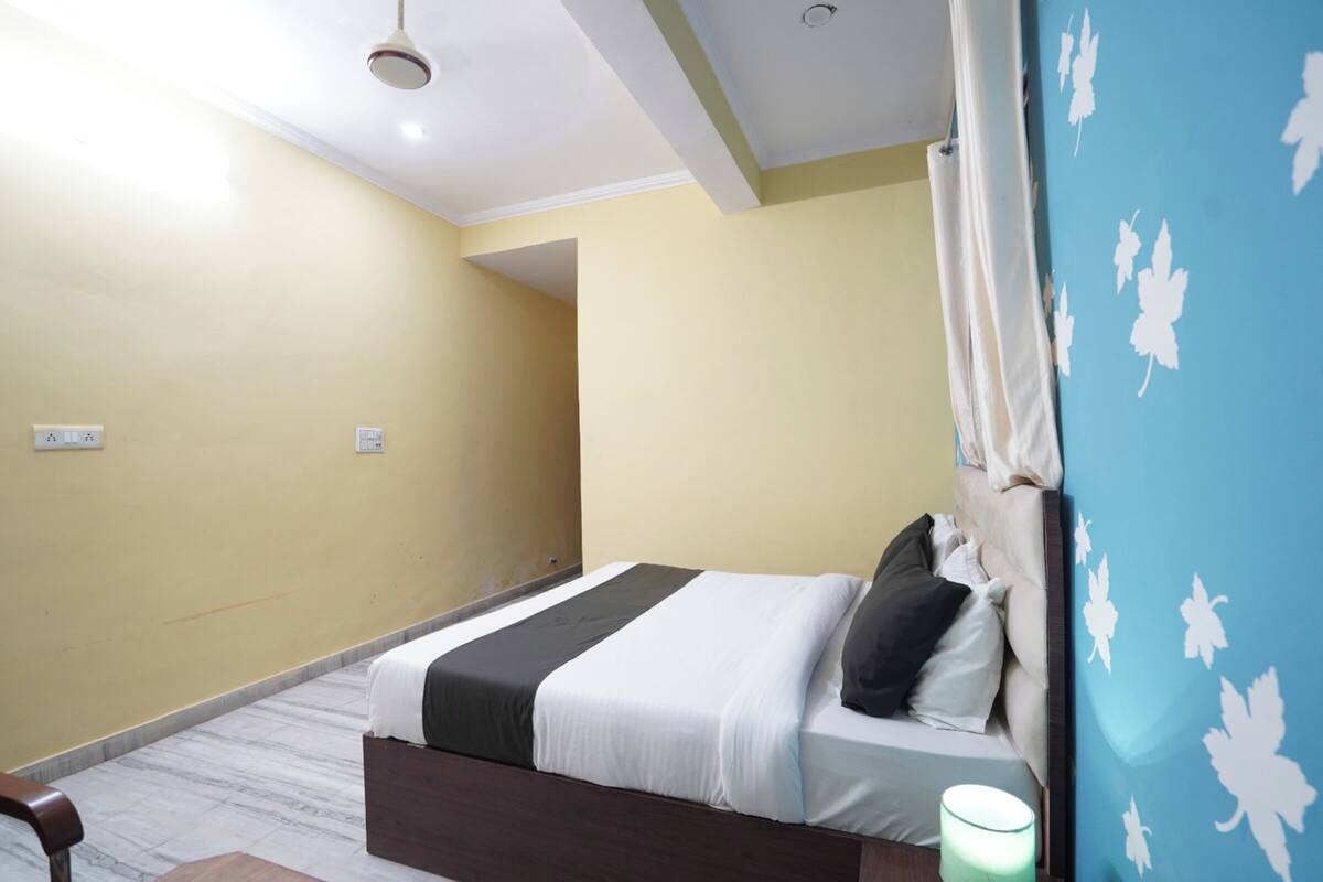 A bedroom with a bed, a bedside table, a lamp, and a wall with a leaf pattern.