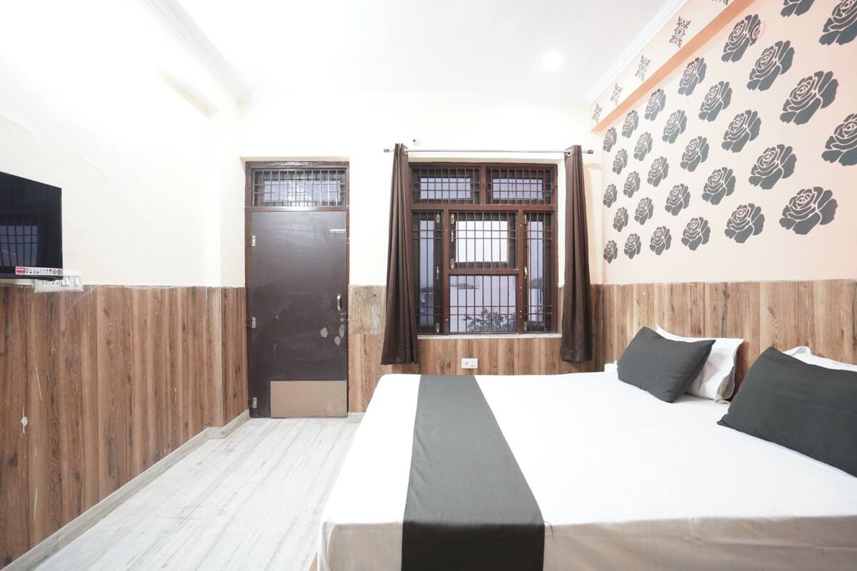 A bedroom with a bed, a wooden door, a window with bars, and a wall with a rose pattern.