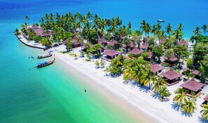 An aerial view of a tropical resort with overwater bungalows, a beach, and a boat dock.