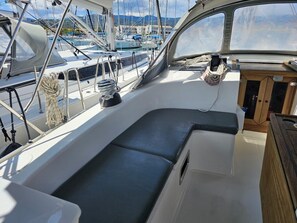 A boat's cabin with a cushioned seating area, a small window, and a door leading to the deck. - Sun-Kissed Sailing Adventure in the Ionian Islands, Lefkada (Lefkada)