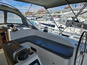 A boat's interior with a cushioned seating area, a wooden side table, and a view of other boats at a marina. - Sun-Kissed Sailing Adventure in the Ionian Islands, Lefkada (Lefkada)