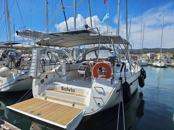 Ein Yachthafen mit einer Segelyacht namens 'Salvia', die an einem hölzernen Deck vor Anker liegt, mit Steuer und Rettungsring.