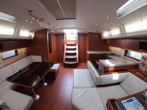 A yacht interior with a dining area, seating, a kitchen, and a staircase leading to an upper deck. - Sun-Kissed Sailing Adventure in Islas Sarónicas (Alimos)