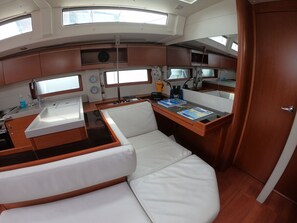 A compact galley with a white sink, a stove, and a small refrigerator. There are two white cushioned seating areas and a wooden countertop. - Sun-Kissed Sailing Adventure in Islas Sarónicas (Alimos)