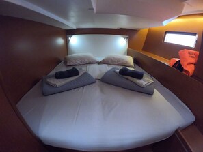 A bed with pillows and folded towels, a headboard, and a window with a view. - Sun-Kissed Sailing Adventure in Islas Sarónicas (Alimos)