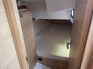 Um espaço interno compacto, com madeira, uma cama beliche, um pequeno armário e uma janela.