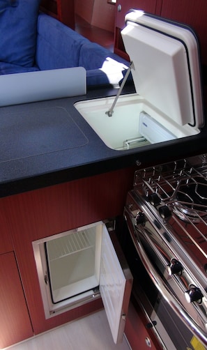 A compact kitchenette with a stove, a small sink, and a window vent.