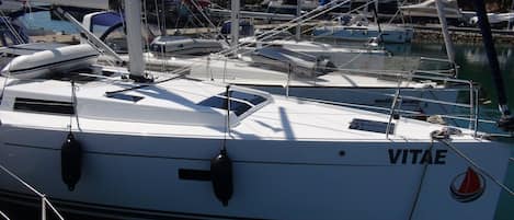 A white yacht named 'VITAE' docked at a marina with other boats.