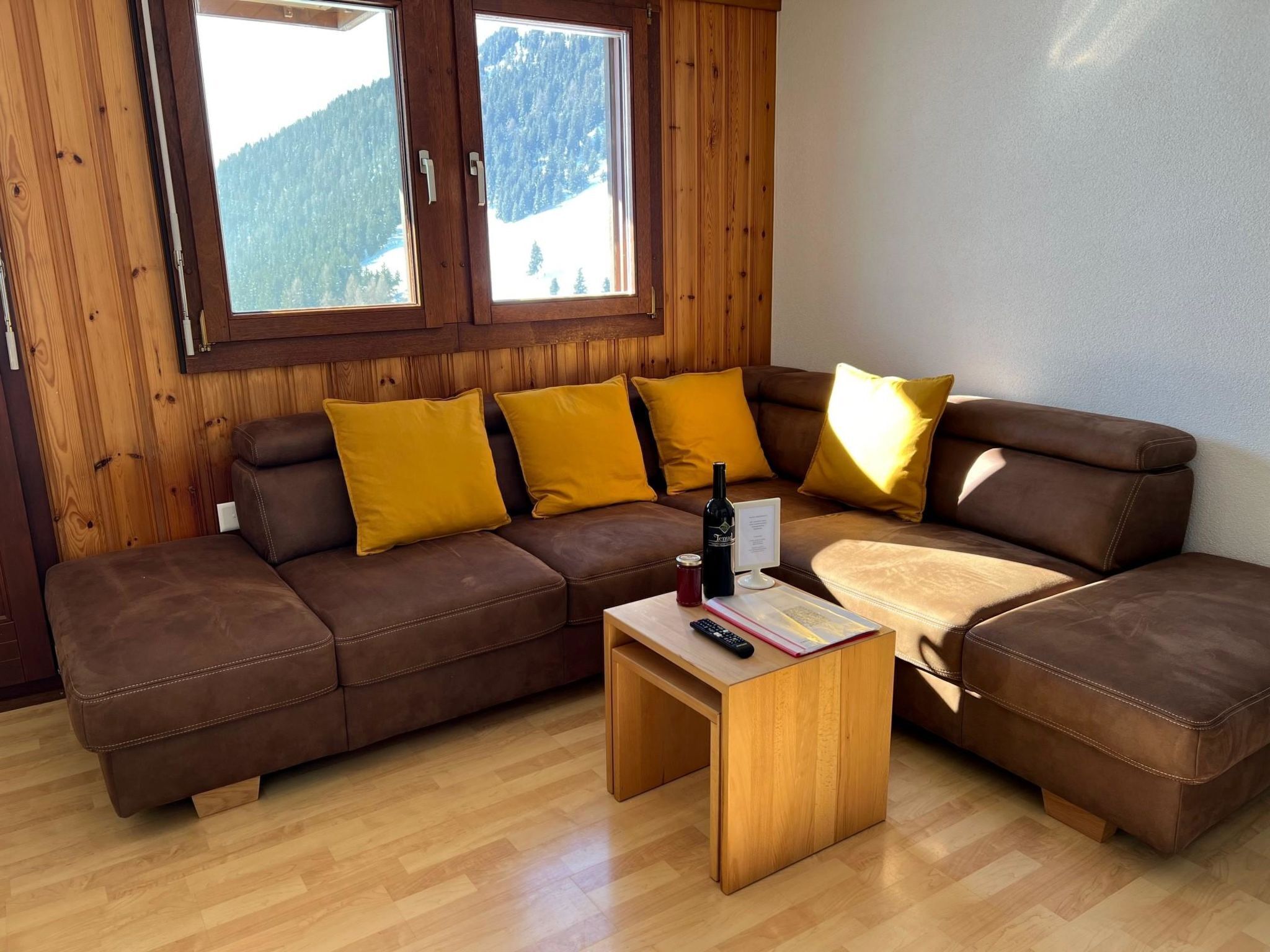 A wooden-paneled room with a brown leather sofa, yellow cushions, and a wooden coffee table with a bottle and remote control.