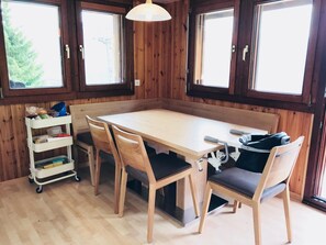 Una habitación con paneles de madera, una mesa y sillas, una lámpara de techo blanca y una ventana con vistas a árboles.