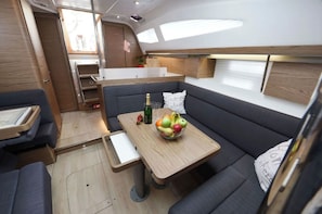 A compact interior with a seating area, a small table with fruit and a bottle, and a kitchenette. - Zadar's Sun-Kissed Sailing Extravaganza: A Croatian Beach Bliss (Sutomišcica)