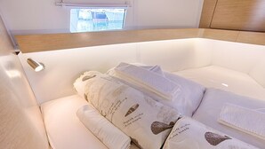 Ein ordentlich bezogenes Bett mit Kissen und einem gefalteten Handtuch, ein Fenster mit Blick auf Boote und ein Holzkopfschild.