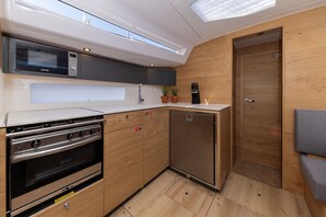 Eine kompakte Küche mit Einbauherd, Mikrowelle und Kühlschrank, Holzschränken und einem kleinen Spülbecken.