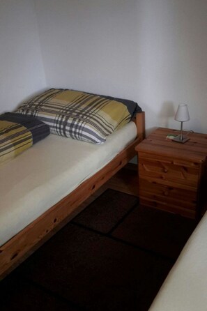 A single bed with a plaid blanket and pillows, a wooden nightstand with a lamp, and a drawer unit. - Konkordia 2 EG Süd-Ost Appartement/Fewo, Dusche oder Bad, WC by Interhome (Bettmeralp)