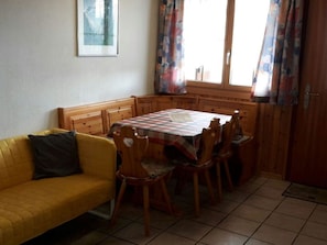 A cozy room with a yellow sofa, wooden dining table, and chairs.