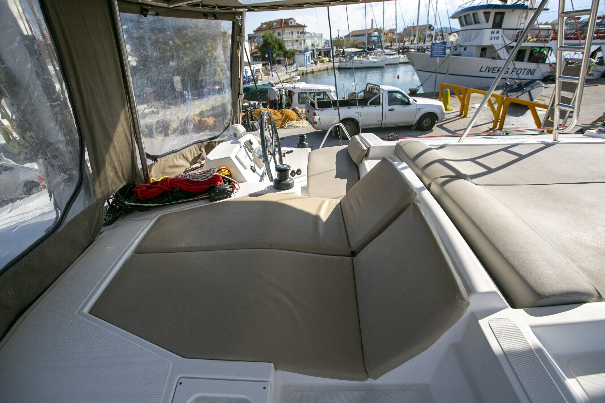 L'intérieur d'un bateau, avec des sièges, un volant et une vue sur la marina, où l'on aperçoit des bateaux et un camion.