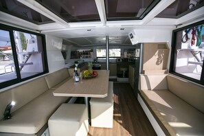 A compact kitchen with a central island, seating area with cushions, and large windows. - Sun-Kissed Sailing Adventure in Egeo Norte - Islas Griegas (Keramoti)