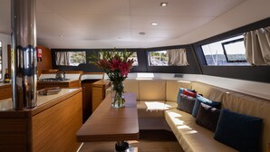A yacht interior with a wooden dining table, a sofa with cushions, a vase with flowers, and a view through the windows. - Sun-Kissed Sailing Adventure in Sibenik, Croatia (Primošten)