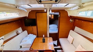 A compact, well-lit interior with a central table, two seating areas with cushions, a small TV, and a window. - Sun-Kissed Sailing Adventure in Sibenik, Croatia (Primošten)