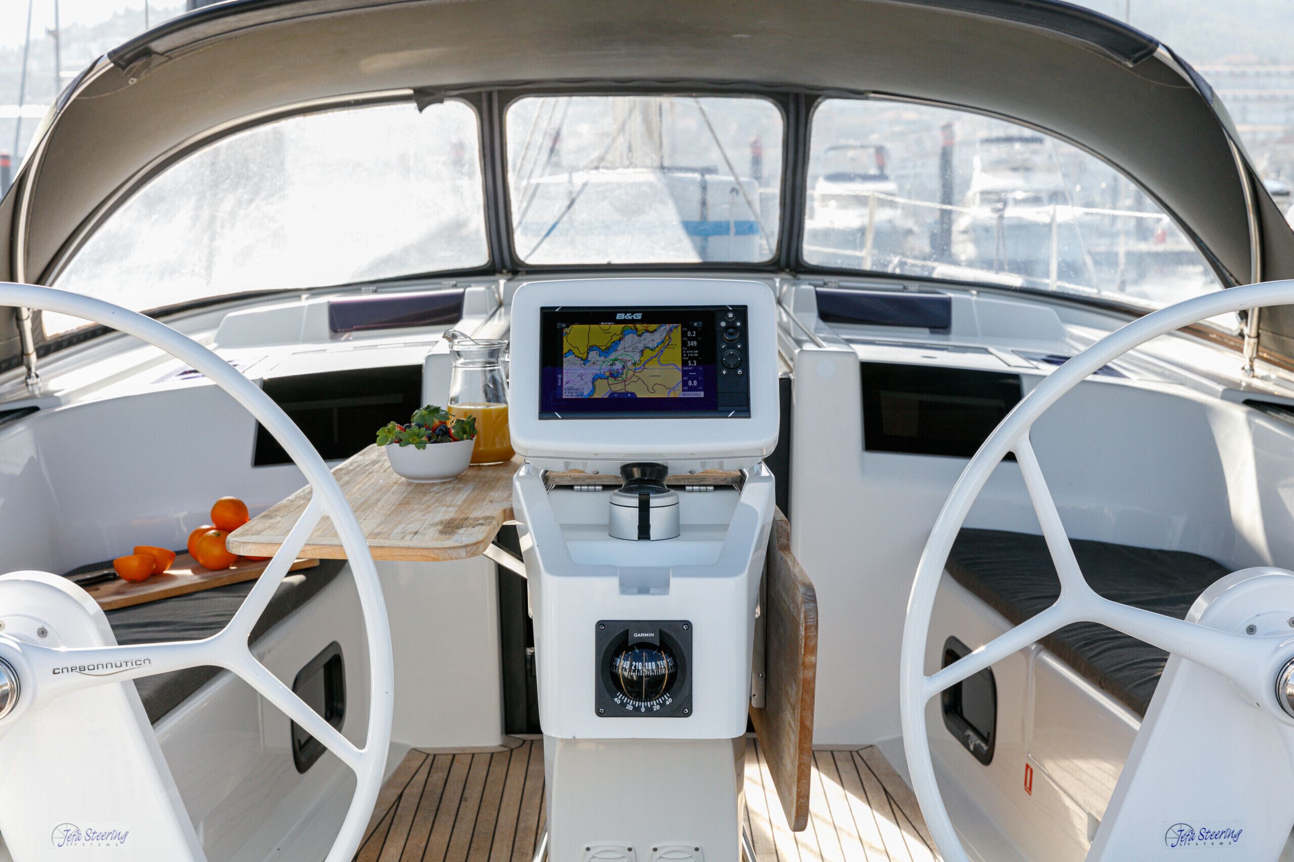 Steuermannstand auf einem Boot mit Navigationsdisplay, Steuerlenkrad und einem Tisch mit Pflanze und Orangen.