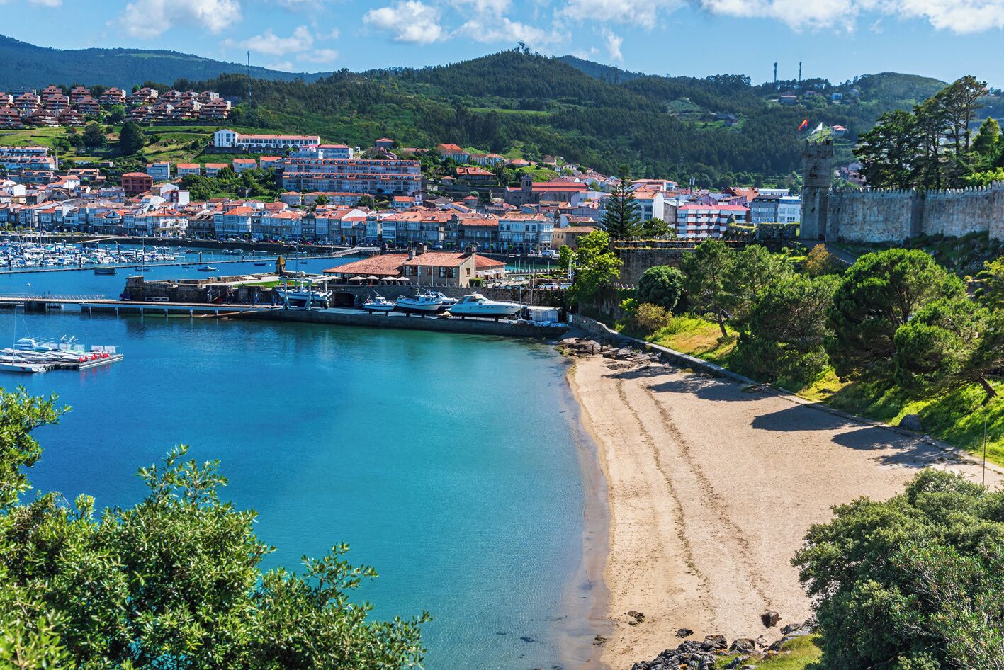 Un pueblo costero con un puerto deportivo, playa de arena y edificios históricos.