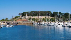 Una marina con barcos amarrados, un castillo en una colina y un edificio con techo rojo.