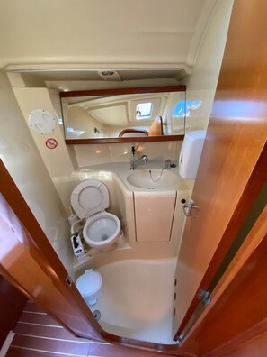 A compact bathroom with a toilet, sink, and mirror. - Sun-Kissed Sailing Adventure in the Ionian Islands, Lefkada (Lefkada)