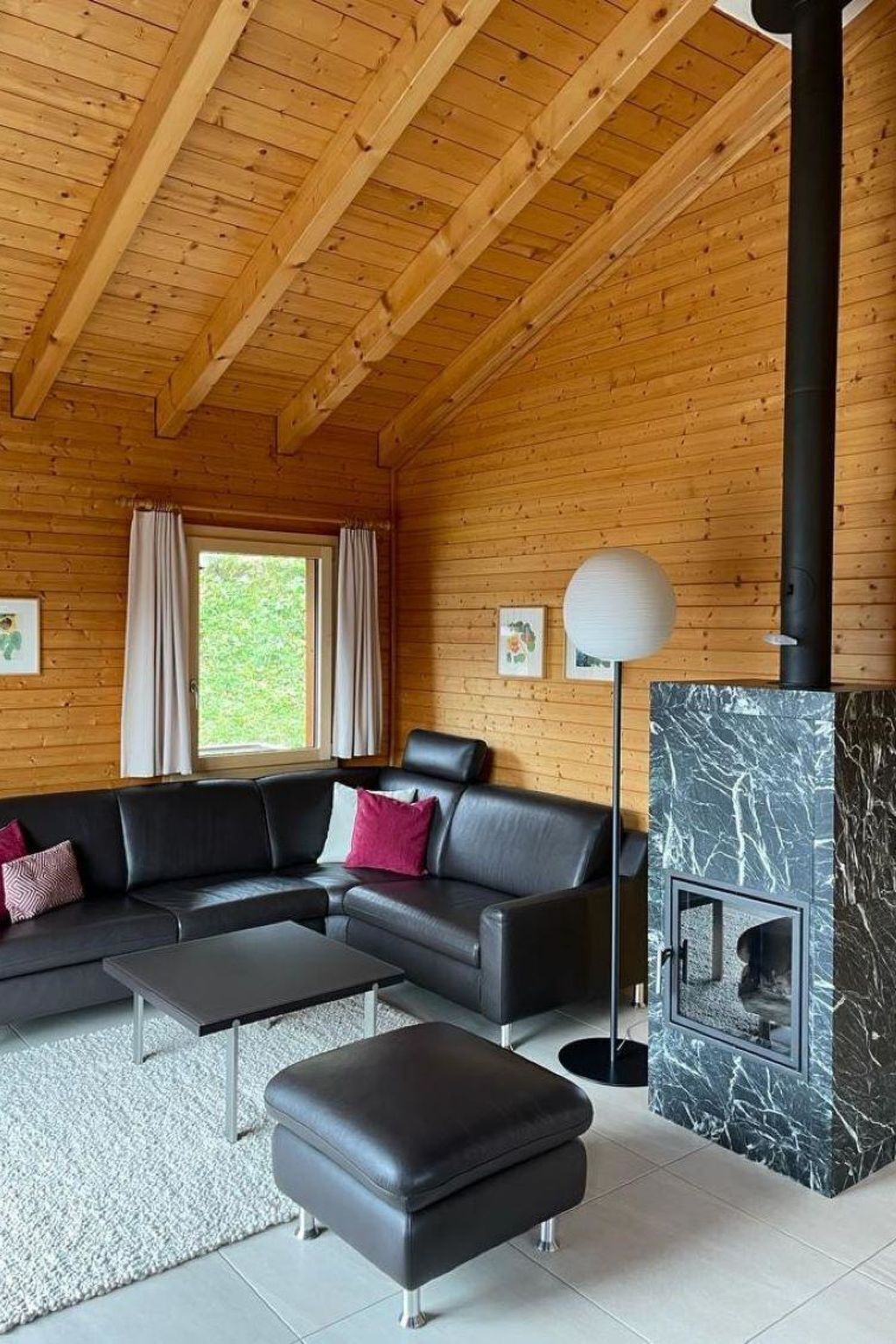 A modern living room with a sectional sofa, a black ottoman, a floor lamp, and a fireplace with a marble surround.