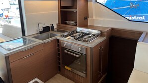 Cocina compacta con estufa a gas, horno y lavamanos, armarios de madera y ventana con vistas a un campo deportivo azul.