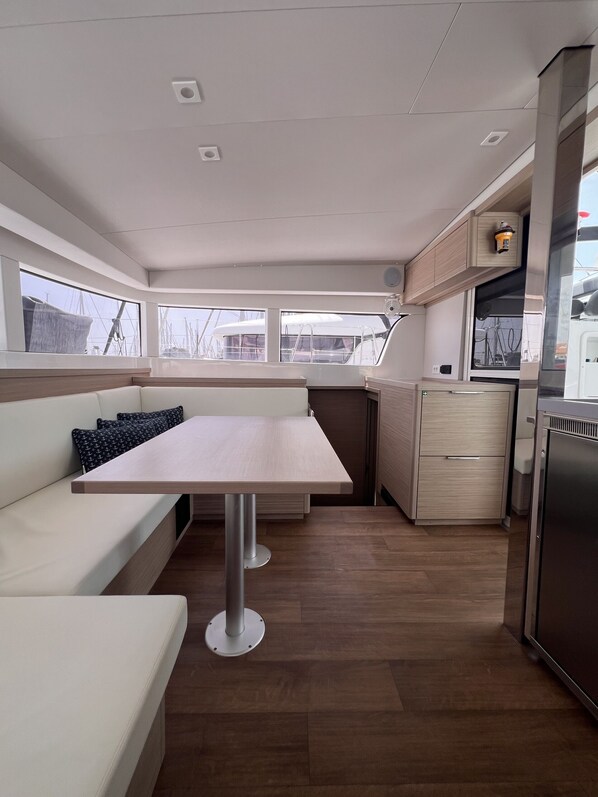 A compact kitchen with a dining area, a built-in refrigerator, and a window overlooking the deck. - Sun-Kissed Sailing Adventure in the Ionian Islands (Kontokali)