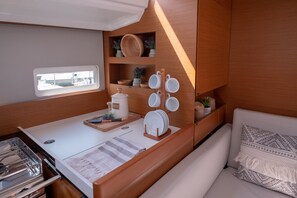 A compact kitchenette with a window, wooden cabinets, and a seating area with a patterned cushion. - Sun-Kissed Sailing Adventure in the Ionian Islands, Lefkada (Lefkada)