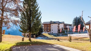 Un bâtiment à étages, une zone pavée au premier plan et une chaîne de montagnes en arrière-plan.