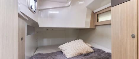 Een compact interieur met een bed, een plafondlamp en een klein raam.