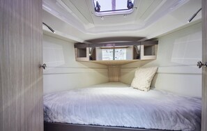 Habitación pequeña y luminosa, con cama, tragaluz y ventana.