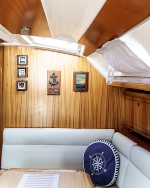 A cabin interior with a wooden wall, a cushioned bench, a compass pillow, and framed pictures.