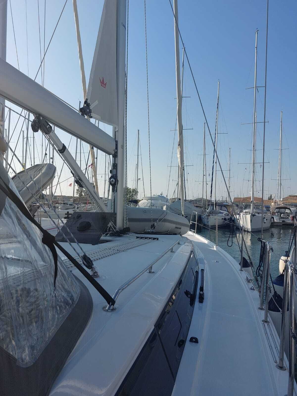 A marina with multiple sailboats docked, a clear sky, and a boat's deck with a steering wheel and navigation equipment.