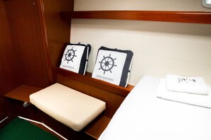 A small cabin with a bed, a wooden shelf with two framed items, and a green carpet. - Sun-Kissed Sailing Adventure in the Ionian Islands (Nikiana)